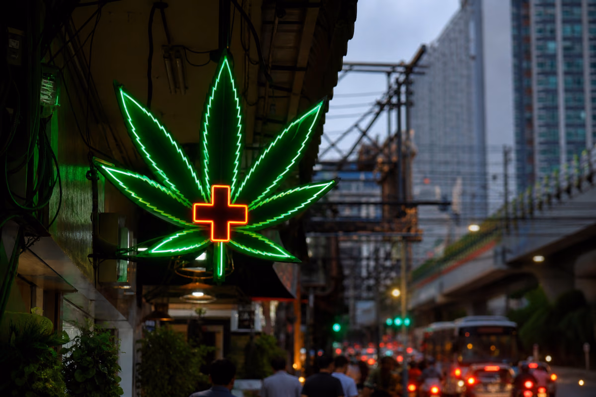 Firmă luminoasă în formă de frunză de cannabis cu cruce medicală deasupra unei străzi aglomerate din Bangkok